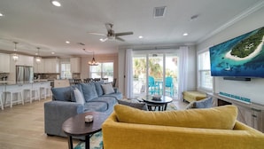A spacious living area with a sofa, a coffee table, and a TV mounted on the wall. There is a kitchen in the background with white cabinets and a dining area with a table and chairs. - ♥ BEACH CONDO ♥ NEW ♥ SLEEPS 10 ♥ 3 BD 2.5 BA ♥ U4 (Indian Rocks Beach)