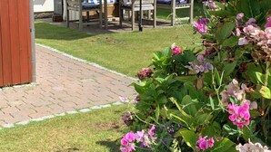 Un patio con mesa y sillas, una sombrilla azul y una maceta con flores rosadas.