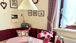 Un comedor con mantel a cuadros, una tetera roja y un jarrón con flores.