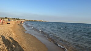 Ein Strand mit Menschen, die spazieren gehen und schwimmen, bewölktem Himmel und ruhiger See.