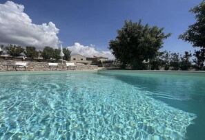 Une piscine aux eaux cristallines, dotée de chaises longues et bordée d’un mur en pierre.