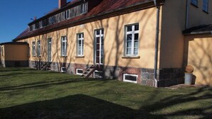 Un bâtiment à deux étages, doté d’une façade jaune et d’un socle en pierre, avec un escalier menant à l’entrée.