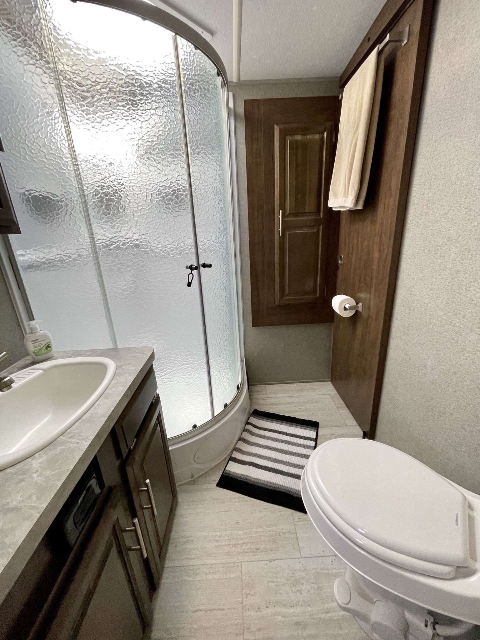Un baño pequeño con un lavamanos blanco, un inodoro y una ducha con puertas de vidrio esmerilado.