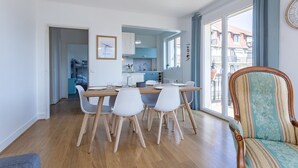 A modern kitchen with white cabinets, a dining table with chairs, and a view of the outside through large windows. - Le Carrousel - Appartement avec studio attenant (Deauville)