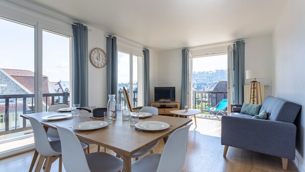 A modern living room with a dining area, large windows, a sofa, and a TV. - Le Carrousel - Appartement avec studio attenant (Deauville)