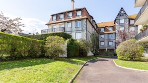 A traditional half-timbered building with a central staircase, surrounded by well-maintained hedges and a clear pathway leading to the entrance. - Le Carrousel - Appartement avec studio attenant (Deauville)