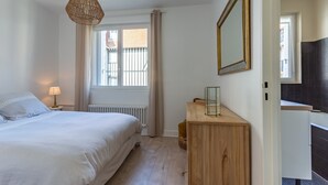 A bedroom with a bed, bedside lamp, wooden dresser, and a mirror. - Le Carrousel - Appartement avec studio attenant (Deauville)