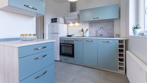 A modern kitchen with light blue cabinets, a white countertop, a built-in oven, a microwave, and a window with a plant. - Le Carrousel - Appartement avec studio attenant (Deauville)