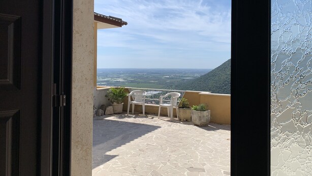 Eine geöffnete Tür, die zu einem Balkon mit Blick auf ein Tal und eine ferne Landschaft führt.