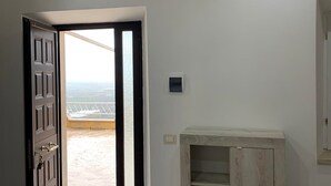 Ein Zimmer mit großer, offener Tür zu einem Balkon, einem Holzkasten und einem Lichtschalter an der Wand.