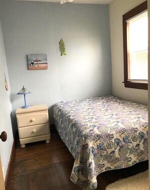 Una camera da letto con un letto, un comodino, una lampada, un quadro e una finestra.