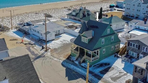 Et kystnært boligområde med huse tæt på stranden, med et markant grønt hus med balkon.