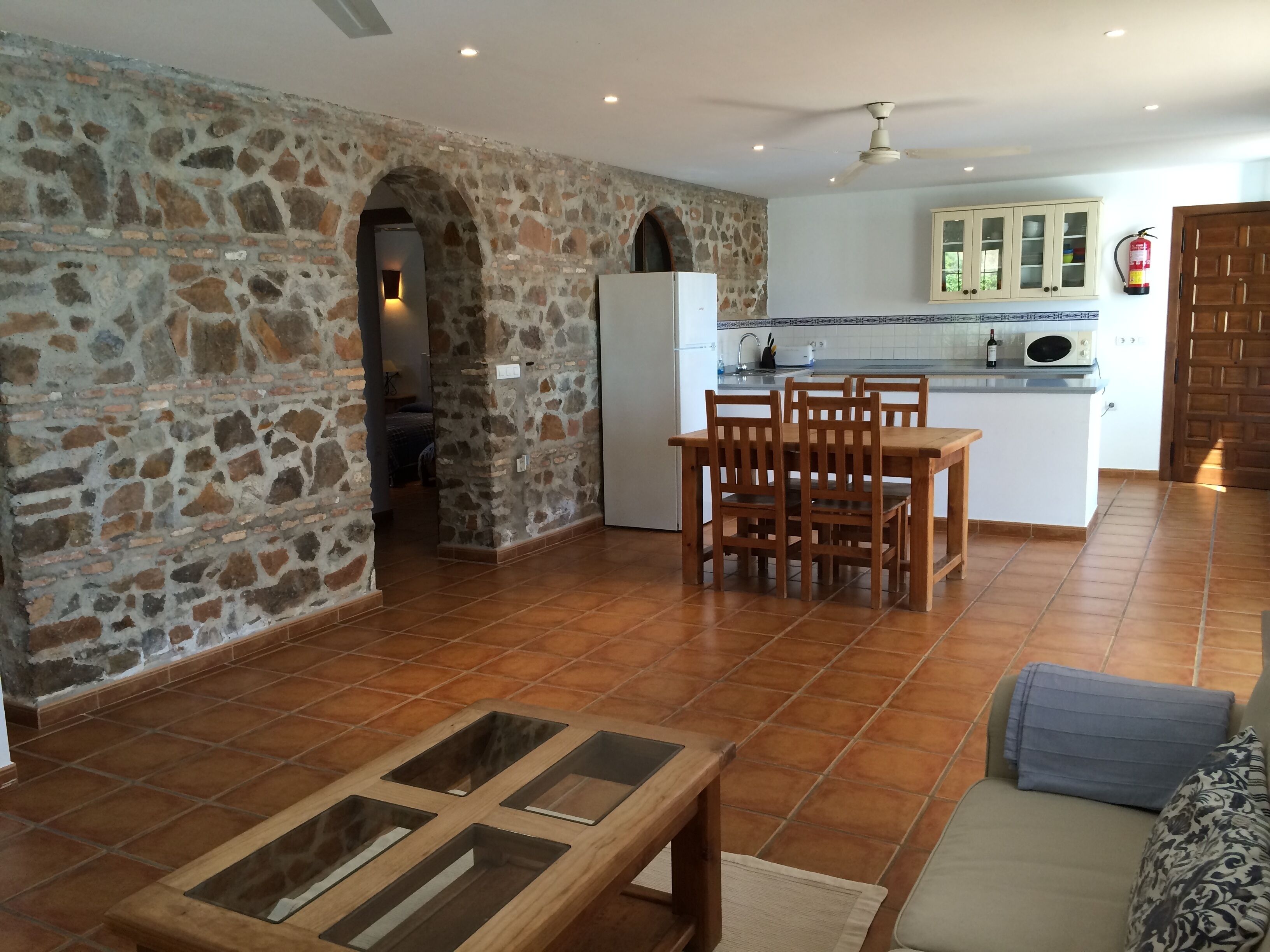 A spacious living area with a stone wall, a wooden dining table, a sofa, and a kitchen in the background.