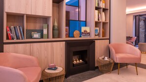 A modern living room with a fireplace, bookshelves, and two pink armchairs. - Hôtel Le Milie Rose (Paris)
