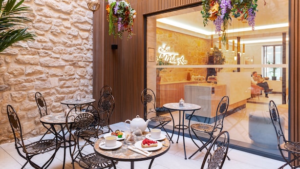 A café with outdoor seating, including tables and chairs, and a visible interior through a glass wall. - Hôtel Le Milie Rose (Paris)