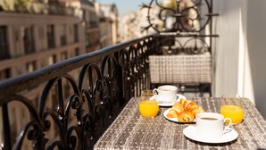 A balcony with a wicker table set for breakfast, including croissants, coffee, and orange juice. - Hôtel Le Milie Rose (Paris)