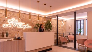A hotel reception area with a stone wall, a receptionist, and modern furnishings including a reception desk, chairs, and a potted plant. - Hôtel Le Milie Rose (Paris)