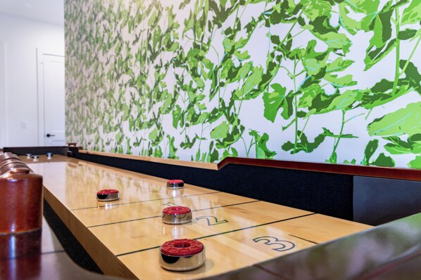 Uma mesa de shuffleboard com três discos, numerados 1, 2 e 3, em um quarto com um mural de parede com folhagem verde.