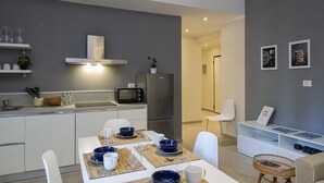 Cozinha moderna com armários brancos, geladeira de aço inoxidável e micro-ondas. Há uma mesa de jantar posta com pratos azuis e brancos.