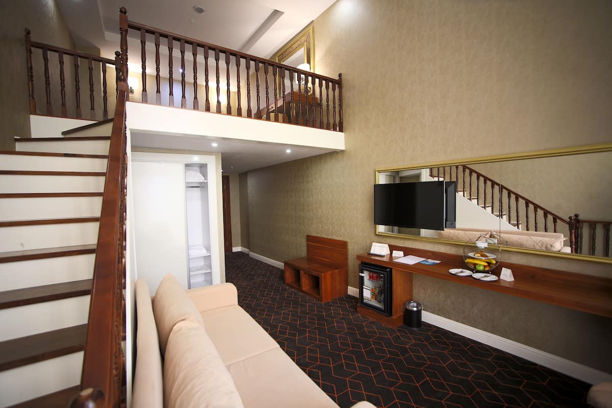 Ein Hotelzimmer mit einer Treppe, einem Sofa, einem kleinen Tisch mit Obstschale, einem Fernseher und einem Spiegel.