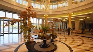 A spacious lobby with a central round table surrounded by potted plants, large windows, and a chandelier. - Terma City Hotel (Termal)