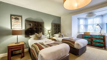 A hotel room with two beds, a wooden nightstand with a lamp, a decorative wall piece, and a window with blinds.