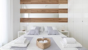 A modern bedroom with a wooden headboard, white bedding, and a wicker basket with towels. - Rivazzurra Homes - 32 (Termoli)