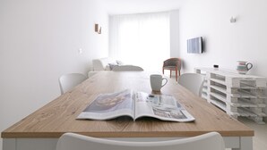A modern, minimalist dining area with a wooden table, white chairs, and a magazine open on the table. - Rivazzurra Homes - 32 (Termoli)