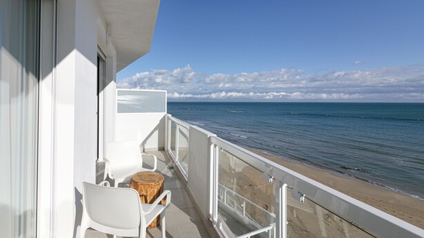 A balcony with white chairs and a wooden stool, overlooking a beach with calm waters and a clear sky. - Rivazzurra Homes - 32 (Termoli)
