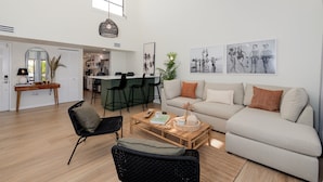 A modern living room with a sofa, coffee table, and chairs. There is a kitchen area in the background with bar stools. - Newly Reno Luxury Condo 30 Steps to Paradise (Clearwater Beach)