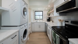 A modern kitchen with a built-in washer and dryer, stainless steel appliances, and a window providing natural light. - Newly Reno Luxury Condo 30 Steps to Paradise (Clearwater Beach)