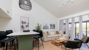 A modern living room with a dining area, a sofa set, a coffee table, and a large window with curtains. - Newly Reno Luxury Condo 30 Steps to Paradise (Clearwater Beach)
