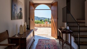 A room with a wooden bench, a table with vases, a painting, and a view of a garden through an open door. - TRADITIONAL  HOUSE. IDEAL FOR FAMILY. PRIVATE  POOL. WIFI WITH FIBER. A/C (Deià)