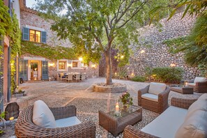 An outdoor patio with wicker furniture, a stone wall, and a tree providing shade. - TRADITIONAL  HOUSE. IDEAL FOR FAMILY. PRIVATE  POOL. WIFI WITH FIBER. A/C. (Deià)