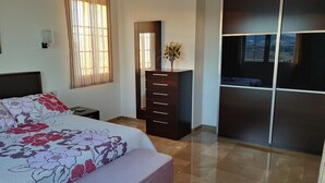 A bedroom with a bed, a dresser, a vanity with a mirror, and a large wardrobe.