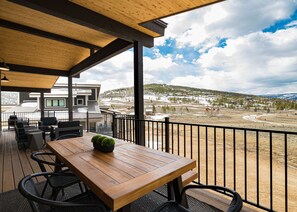 A wooden deck with a table and chairs, overlooking a snowy landscape with buildings and trees. - Lone Eagle Chalet at Granby Ranch - With Hot Tub! (Granby)