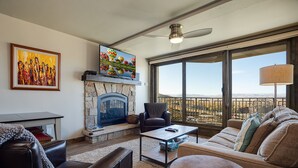 Una sala de estar con chimenea de piedra, un sillón de cuero, un sofá y un ventanal con vistas a las montañas.