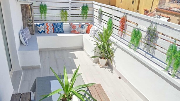 A rooftop terrace with a wooden bench, potted plants, and colorful cushions.