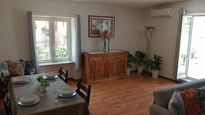 A dining area with a wooden table set for four, a sofa, and a cabinet with plants.