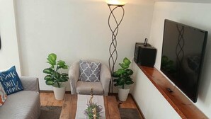 A cozy living room with a sofa, a coffee table with a decorative centerpiece, a floor lamp, and a flat-screen TV mounted on the wall.