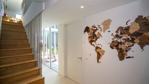 Et moderne interiør med en trappe i træ, en glasdør der fører til et lyst rum, og et verdenskort på væggen.