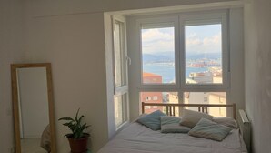 A bedroom with a large bed, a potted plant, a mirror, and a view of a cityscape through a large window. - Balcón a la Bahía. Bay Views (Santander)