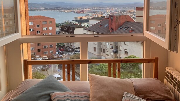 A bedroom with a large window offering a city view, a wooden headboard, and multiple pillows. - Balcón a la Bahía. Bay Views (Santander)