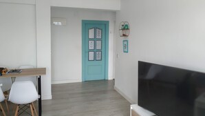 A modern living room with a teal door, a flat-screen TV, and a dining area with a wooden table and white chairs. - Balcón a la Bahía. Bay Views (Santander)