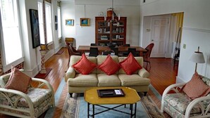 A spacious living room with a beige sofa, two armchairs, a coffee table, and a dining area with a wooden table and chairs.