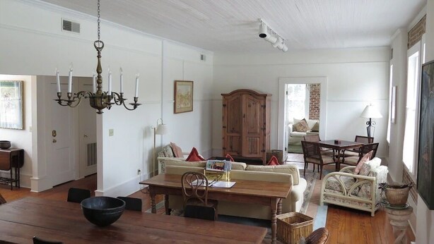 A spacious living room with a wooden dining table, a sofa, and a chandelier.