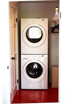 Laundry room with a front-loading washing machine and a red tiled floor.