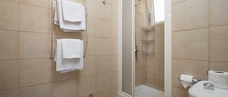 Un baño con azulejos color beige, ducha, inodoro y un perchero con toallas dobladas.