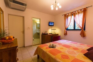 Habitación de hotel con cama, escritorio, televisor y ventana con cortinas.