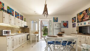 A modern kitchen with white cabinetry, a dining area with blue chairs, and various colorful artworks on the walls.